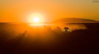 машина поднимает дорожную пыль, создавая интересные условия для закатной фотосессии.