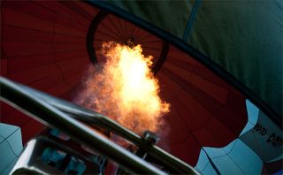 Вообще, должен сказать, что полёты - сплошное надувательство ... Собственно «горелка» — тепловая система аэростата, нагревающая снизу воздух в оболочке шара с помощью открытого пламени, состоит из двух горелок: рабочей и дежурной. Узкое и длинное пламя от рабочей горелки возникает от сгорания жидкого газа, глубоко проникает внутрь оболочки и обеспечивает высокий КПД тепловой системы. Включается рабочая горелка периодически. Шум от нее — большая проблема, его уровень может составлять примерно 100 дБ. Рев горелки заглушает речь и на расстоянии 200 метров способен заставить обратиться в паническое бегство целое стадо коров. Дежурная горелка питается обычным газом, горит постоянно и держит спираль, по которой газ в разогретом состоянии поступает в рабочую, что и обеспечивает выброс пламени из рабочей горелки. Кстати, треугольный фартук, обычно прикрепляемый между корзиной и оболочкой с одной из сторон шара, предназначен для того, чтобы порыв встречного ветра не погасил дежурную горелку.