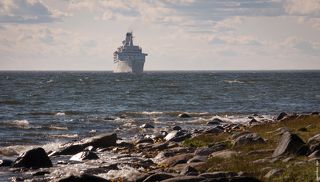 из-за того что окрестности Соловков весьма мелководные, пришлось этому огромному лайнеру встать на рейде поодаль, а интуристических пассажиров возить на берег на спасательных шлюпках.
(Тут телевик существенно сжал расстояние, корабль на самом деле весьма далеко стоял.)