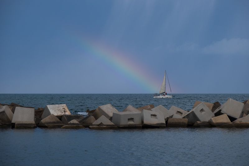 barcelona coast, coastal beauty, concrete block division, sailboat, rain and rainbow, nature and urban charm, mesmerizing scene, barcelona maritime scenery, sky, captivating composition, vibrant coastal panorama, natural wonders of barcelona, urban coasta Sailboat Splendor: Barcelonaphoto preview