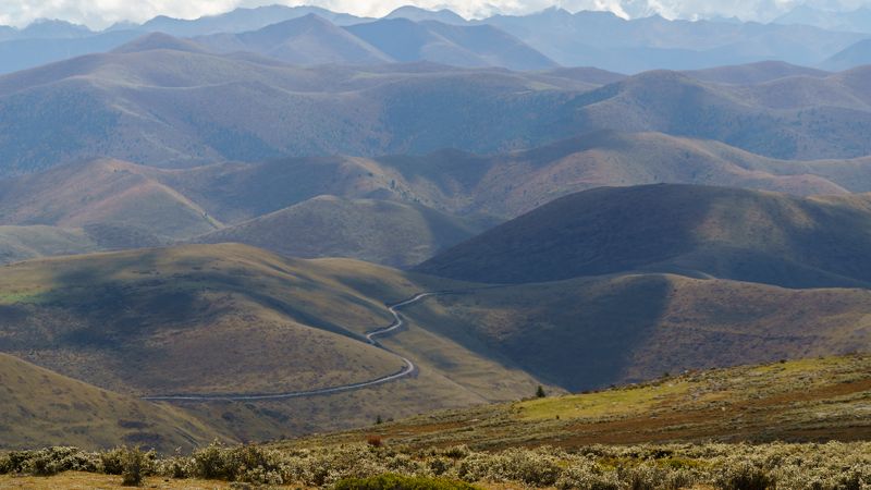 high hills, mountain valley, asphalt road, grey snake road, tall mountains, white snow mountains, green hills, blueish fog, foggy valley, rare bushes, scenic landscape, mountainous terrain, serpentine road, misty valley, breathtaking view Mountain Serenityphoto preview