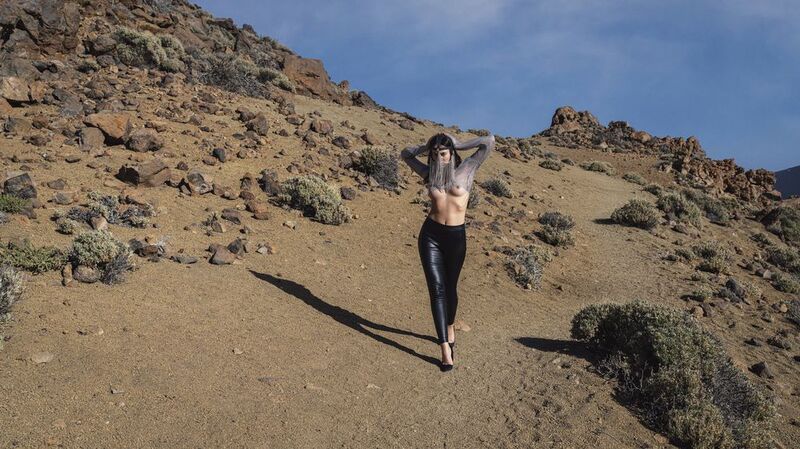artistic nude, beauty in nature, body confidence, contrasting light, desert, el teide, elegance, expressive stance, front view, grace, looking at camera, mask, naked, one person, outdoors, rocks, sand, sensuality, skies, trousers, walking, young woman A Vision in the Desertphoto preview
