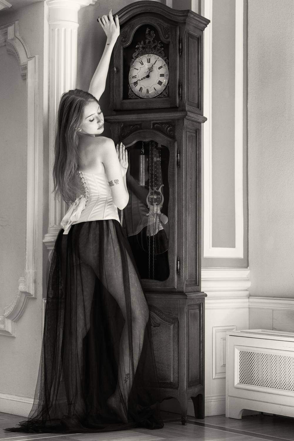 Melancholy and Time. Автор: Alex Tsarfin artistic nude, back view, beautiful woman, corset, dark romanticism, elegant pose, feminine grace, grandfather clock, modern muse, monochrome, nostalgic, one person, quiet sensuality, reflection, sheer fabric, standing, vintage aesthetic, young woman, Alex Tsarfin