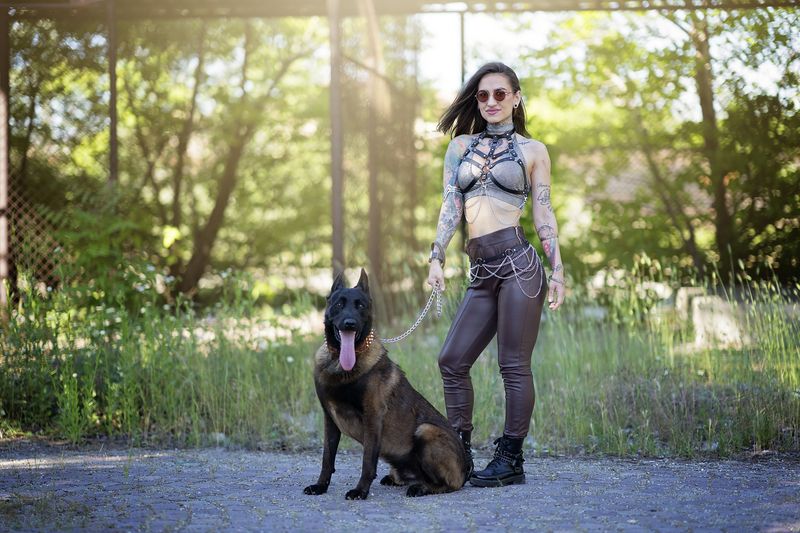 tattooed woman, Belgian Malinois, chains, alternative style, urban fashion, attitude, female power, nature-city contrast, sunlight, dominance, portrait photography, gothic style, urban forest, edgy look, outdoor fashion Urban Commandphoto preview