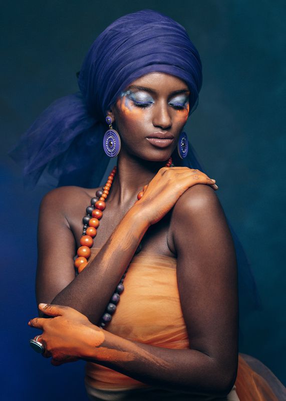 amber accents, artistic portrait, blue backdrop, cinnamon shadows, contrasting light, delicate pose, desert muse, eastern adornment, exotic elegance, female portrait, front view, golden hues, makeup, oriental portrait, vintage orientalism, young woman Jewels of the Caravanseraiphoto preview