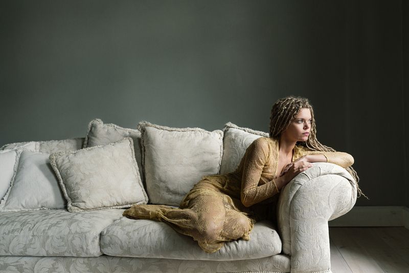 artistic portrait, braided hair, delicate fabric, elegant pose, emotional stillness, golden dress, interior minimalism, introspective gaze, muted palette, neutral décor, restful poise, serene composition, soft light, soft shadows, textured couch The Hour Between Momentsphoto preview
